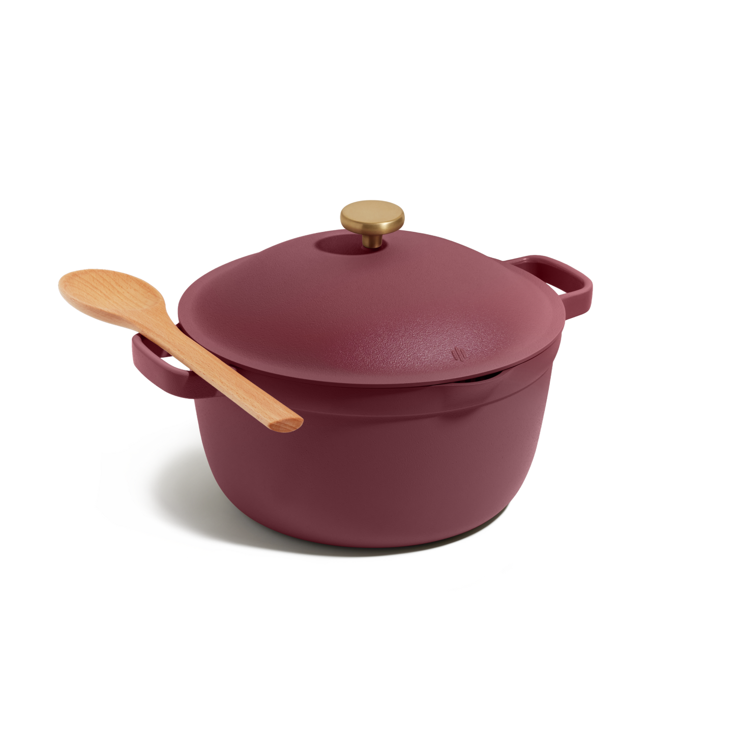 The Perfect Pot, a maroon cast iron Dutch oven with a gold knob, is displayed on a white background with a wooden spoon resting on its lid. This versatile pot is ideal for family meals.